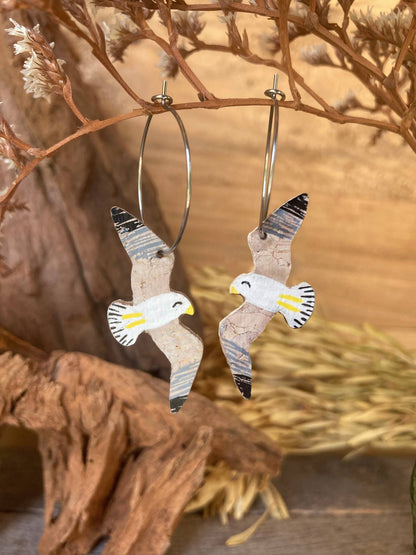 Seagull earrings with little yellow legs and beak made from cork hanging from a natural branch