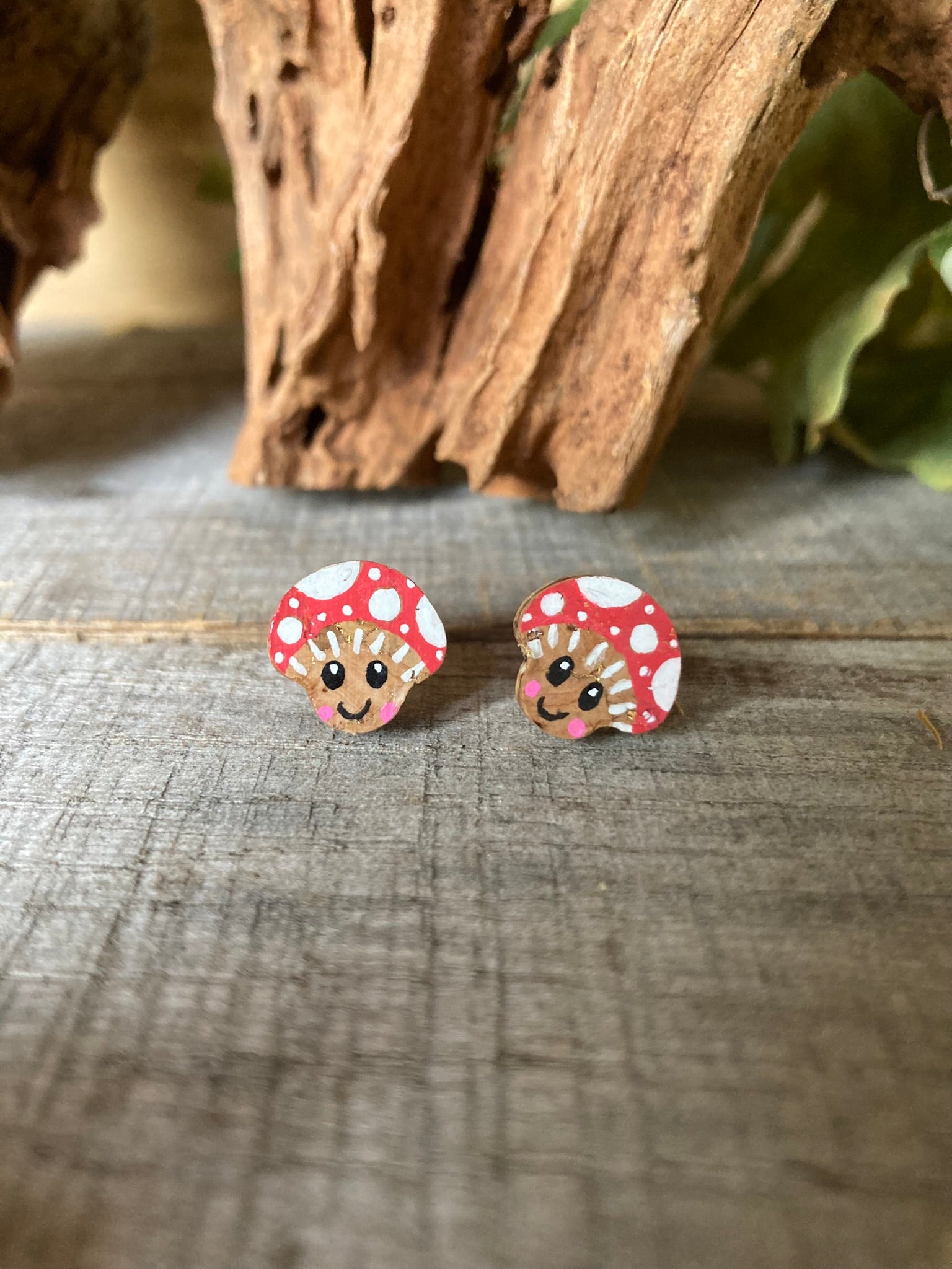 Pair of happy toadstool-shaped stud earrings with red caps and white spots on a wooden surface.