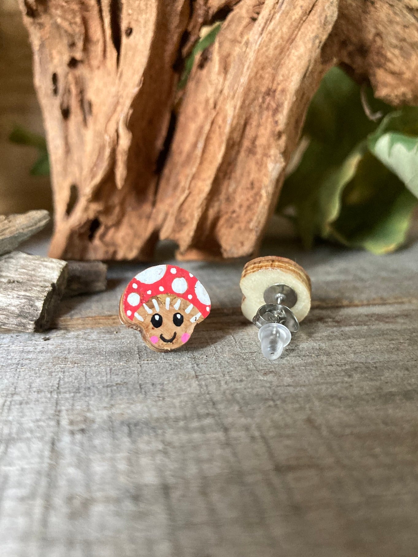 Two mushroom-shaped earrings on a wooden surface with a natural background. One facing forwards and the other showing the back. Back is made from plywood with a metal butterfly and rubber stud fastenings