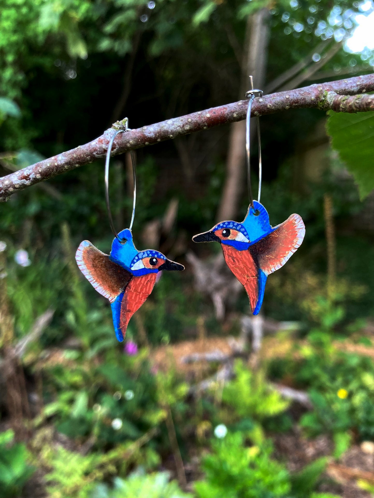 Colorful bird-shaped earrings hanging on a branch with a natural green background