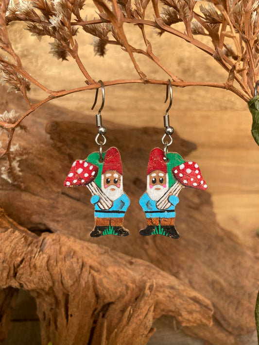 Gnome earrings with red hats and red toadstools on a wooden surface.