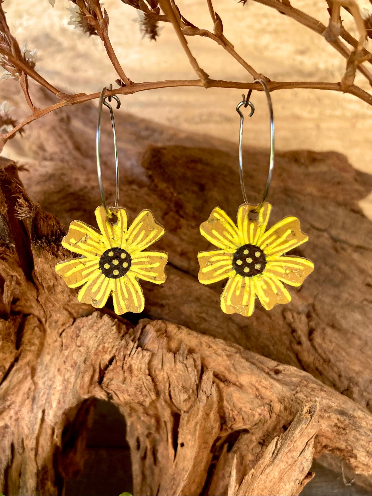 Yellow abstract sunflower-shaped hoop earrings on a wooden surface with a natural background