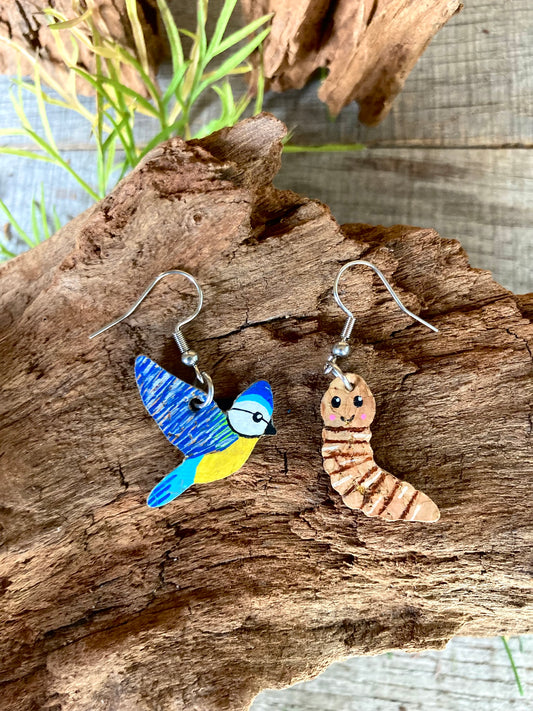 Bird and worm earrings on a wooden surface