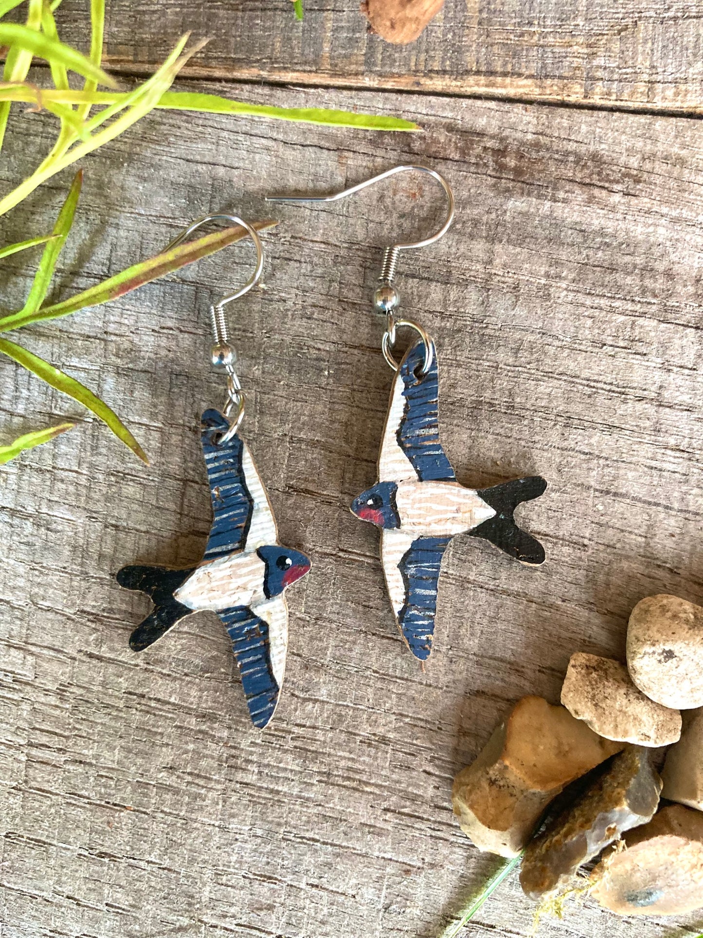Bird-shaped earrings on a wooden surface with natural elements.
