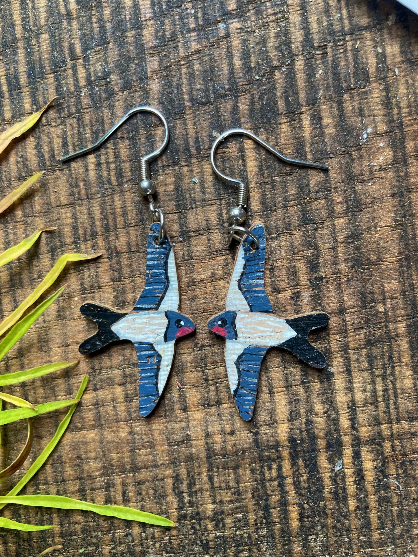 Pair of swallow-shaped earrings on a wooden surface with leaves.