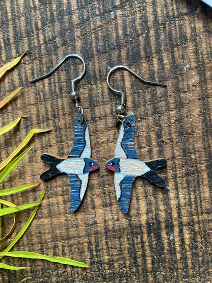 Pair of swallow-shaped earrings on a wooden surface with leaves.