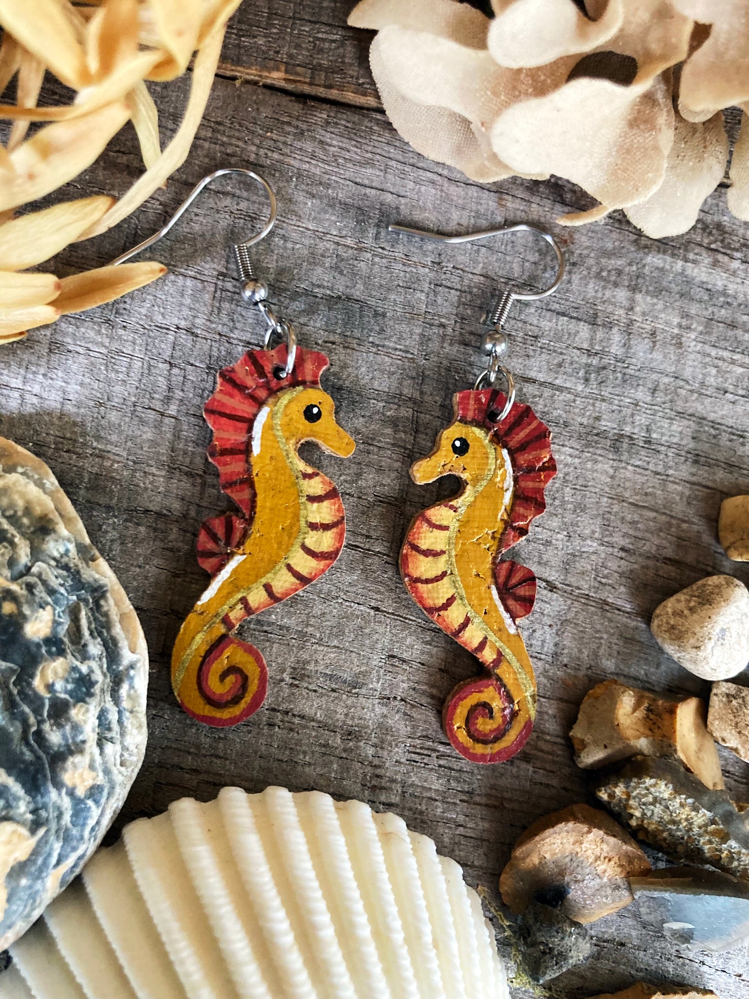 Seahorse earrings on a wooden surface with seashells and stones.