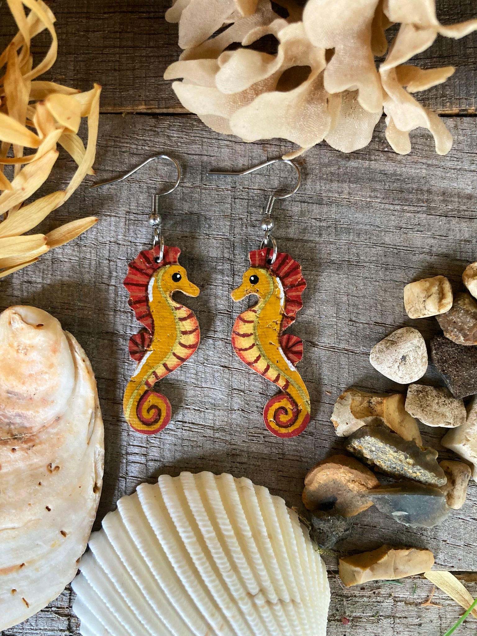 Seahorse earrings on a wooden surface with seashells and rocks