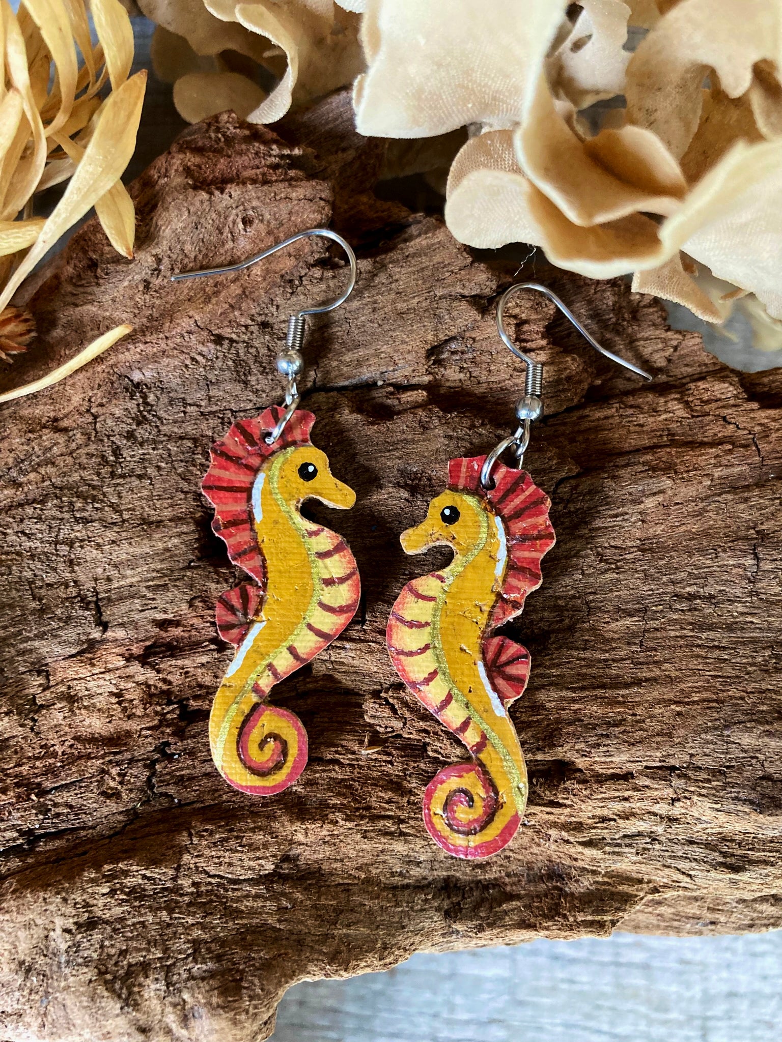 Seahorse earrings on a wooden surface with flowers in the background