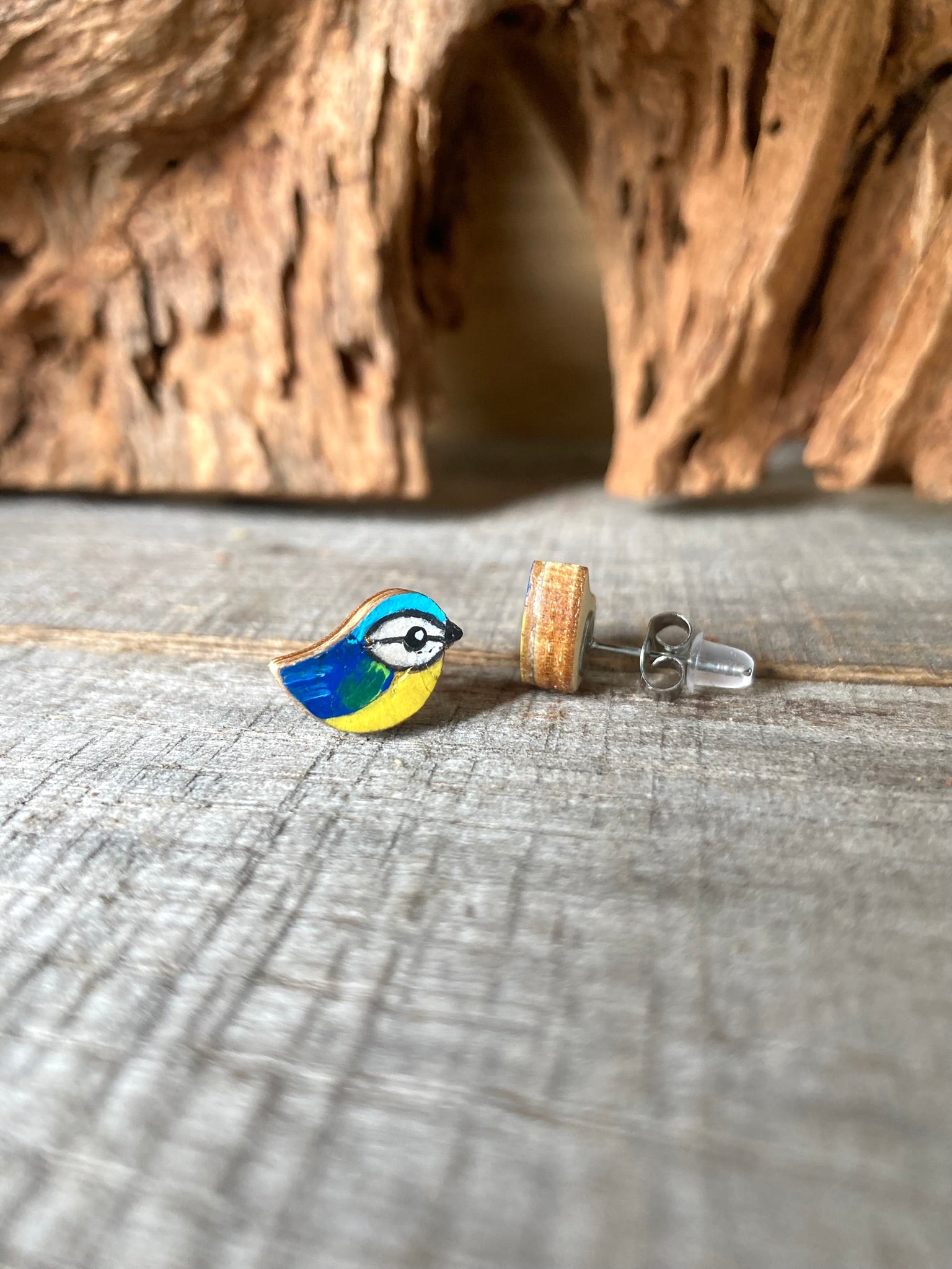 Bird-shaped earrings on a wooden surface with a natural background. Secured with a metal butterfly back and rubber back