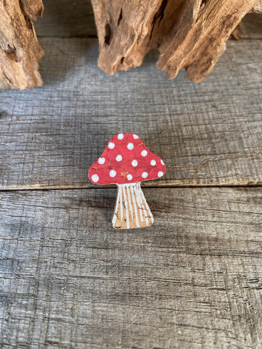 Decorative mushroom pin badge with a red cap and white polka dots on a wooden surface