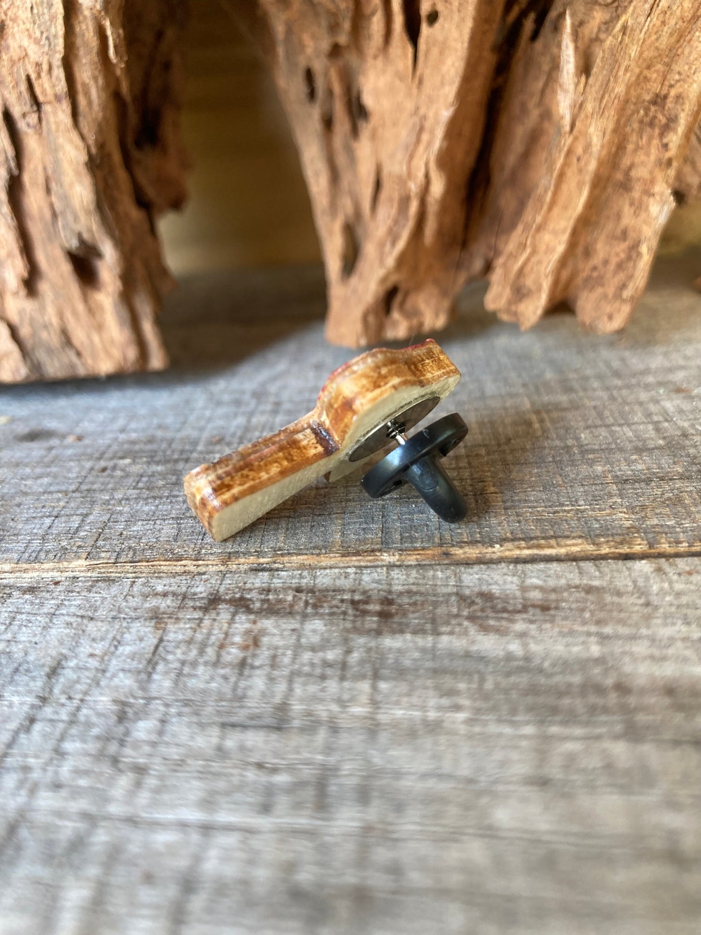 Small wooden pin badge with a black rubber back on a rustic wooden surface