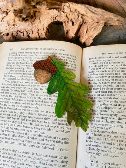 Open book with a leaf and acorn bookmark on a wooden surface