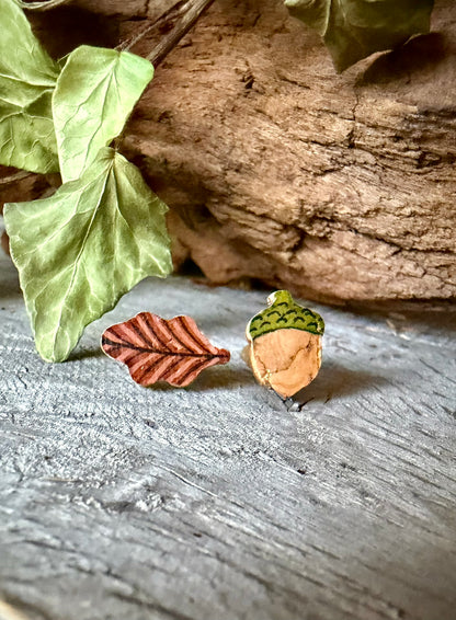 Acorn and oak leaf cork stud earrings on weathered driftwood with ivy, showing russet leaf and gold fleck acorn with olive green cap