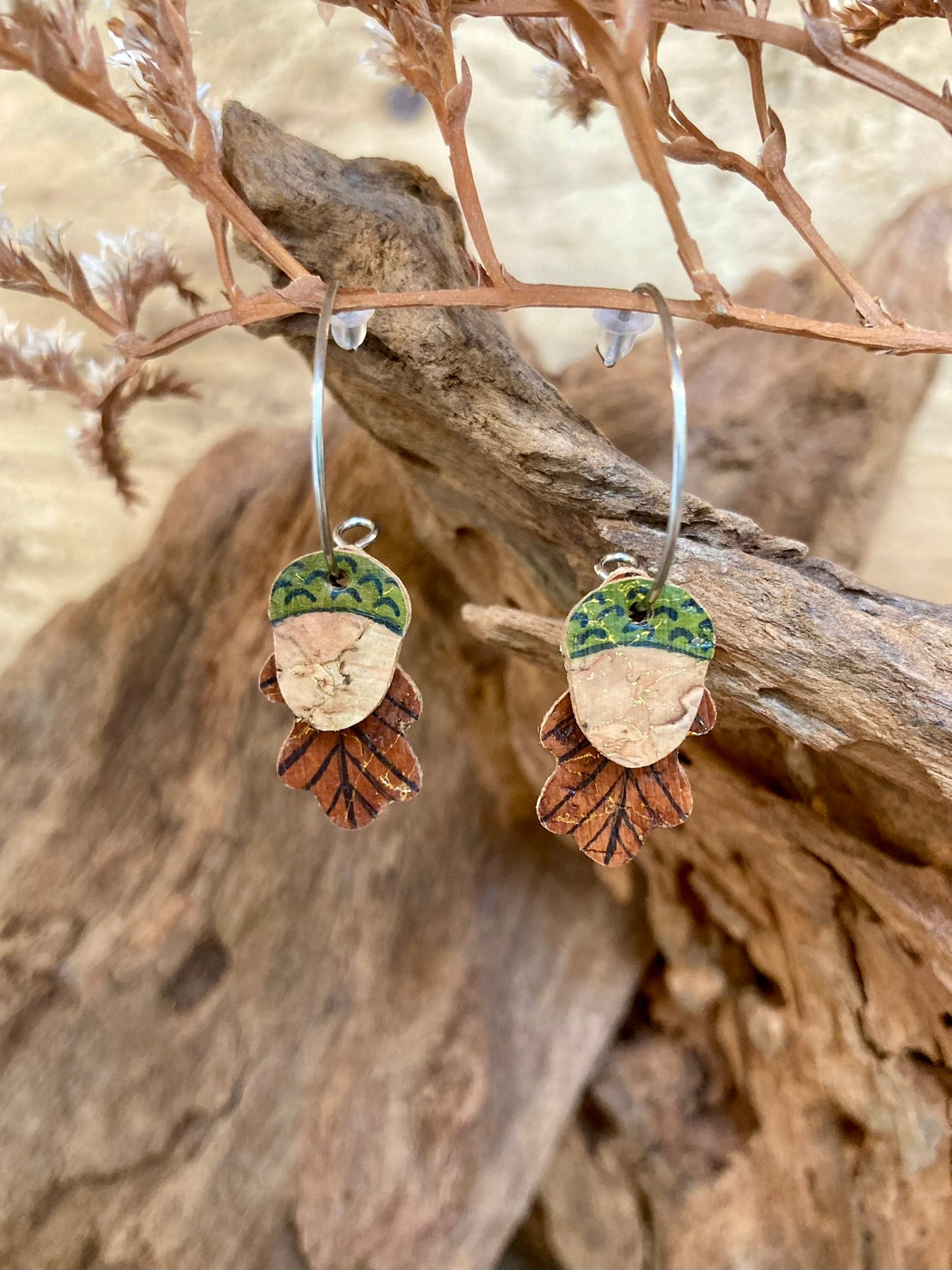 Cork acorn and oak leaf earrings hanging from a dried russet branch against a warm autumnal background