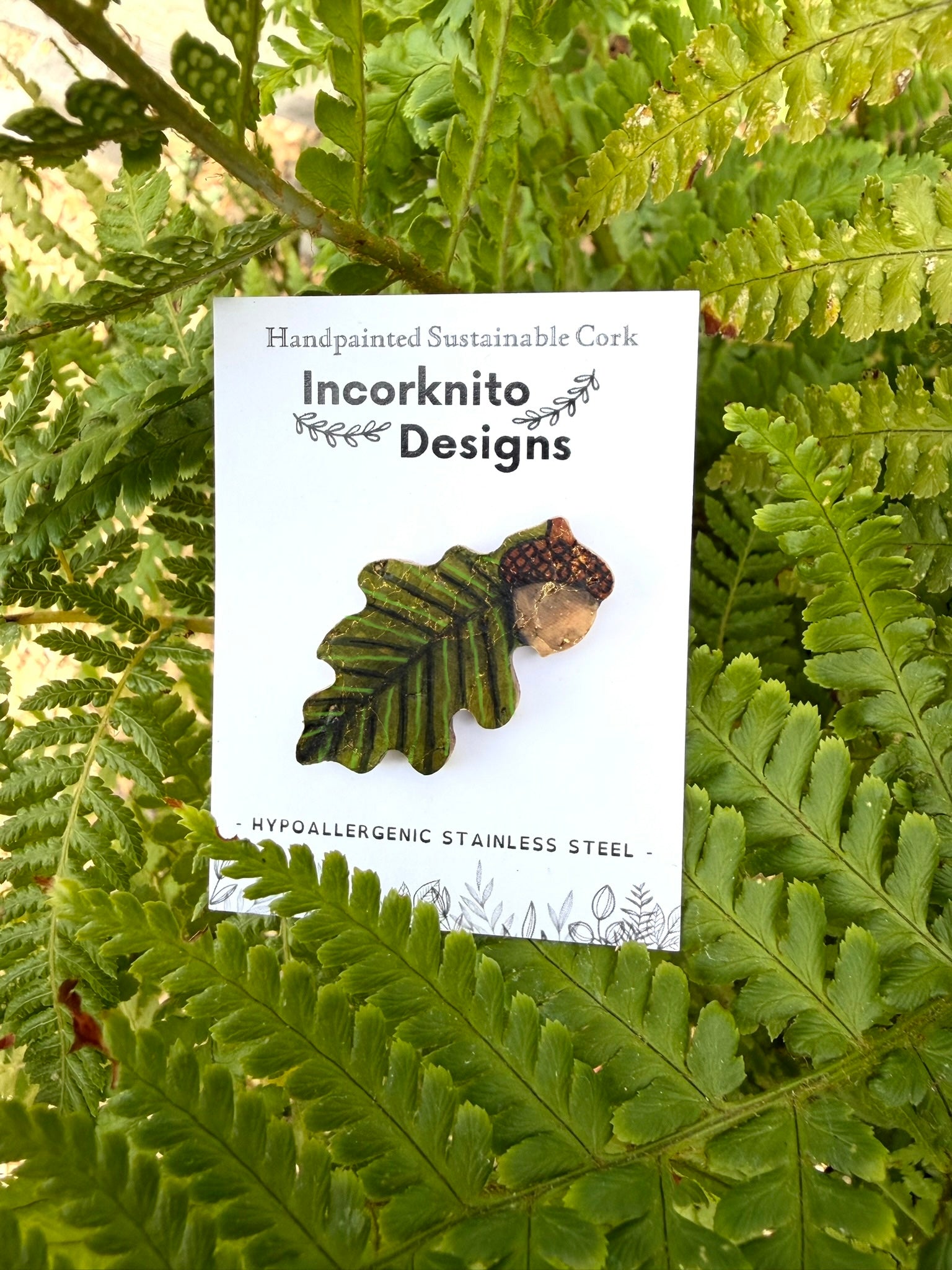 Acorn and oak leaf cork pin badge on Incorknito Designs branded card against green fern fronds — handpainted sustainable badge handmade in UK