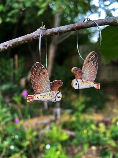 Handpainted barn owl cork earrings on silver hoops hanging from a woodland branch 