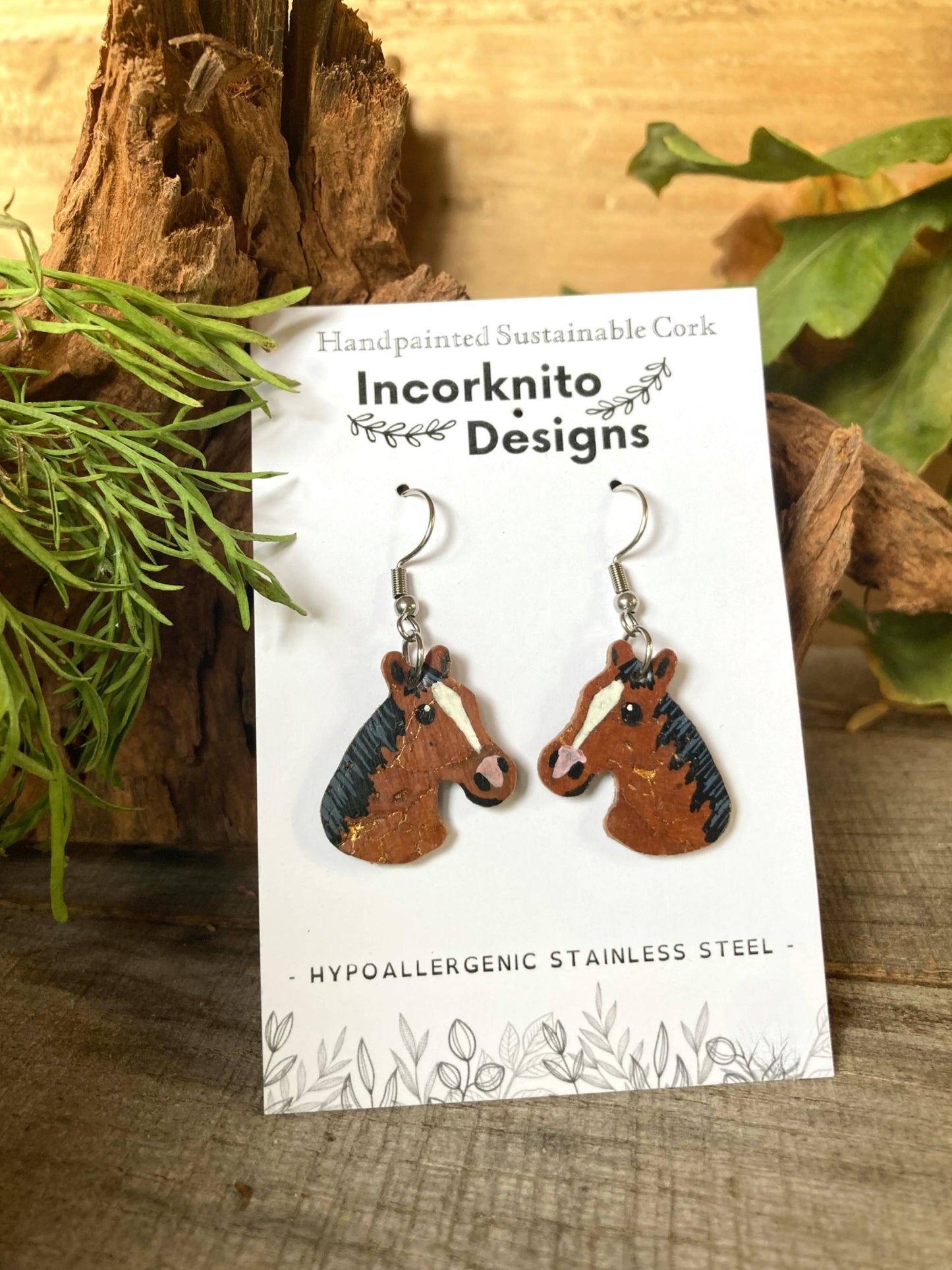 Bay and brown horse cork earrings on silver hooks on Incorknito Designs branded card against natural wood and greenery — handpainted sustainable cork jewellery