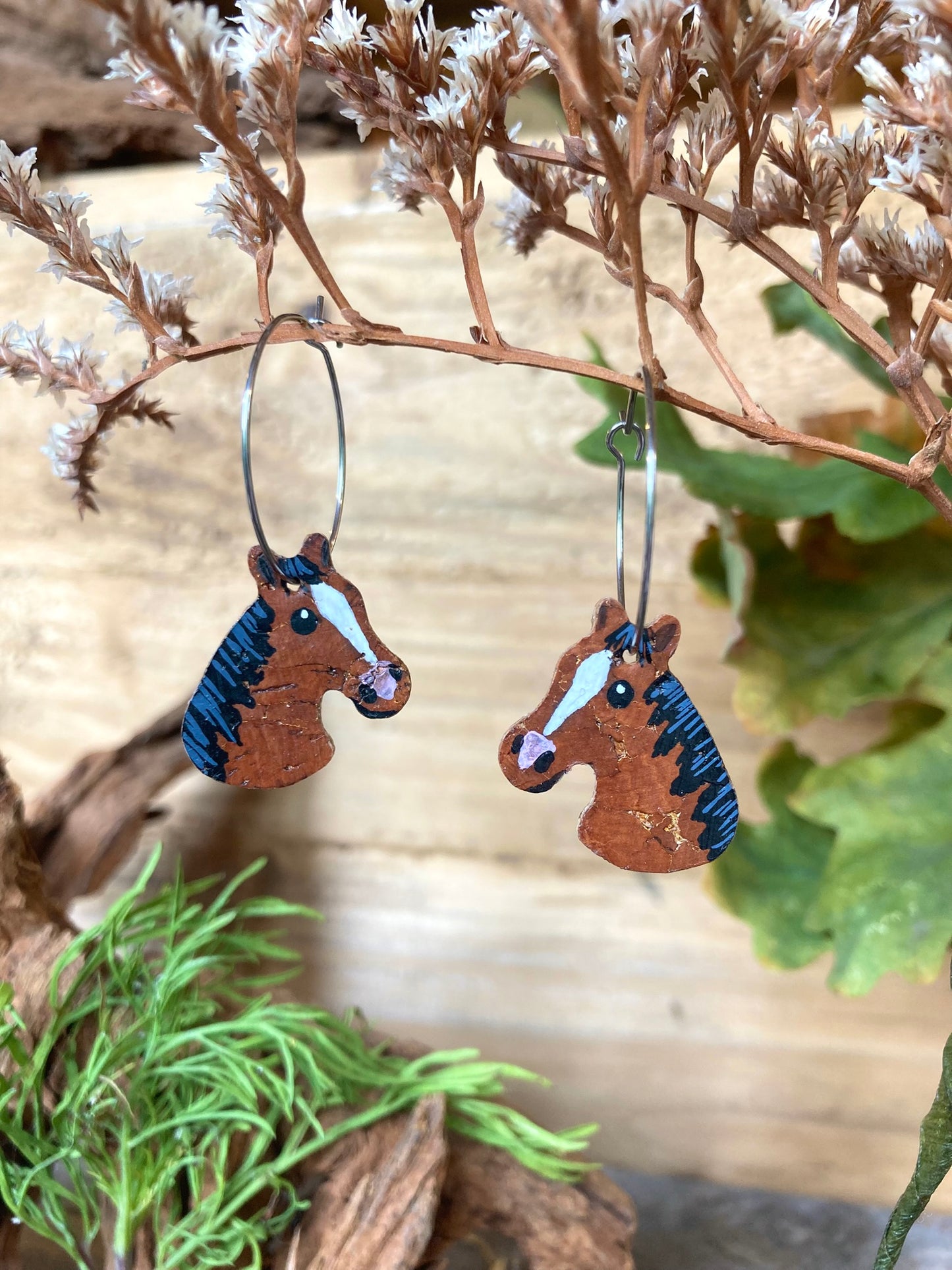 Handpainted bay horse cork earrings on silver hoops hanging from a dried botanical branch — sustainable cork equestrian jewellery