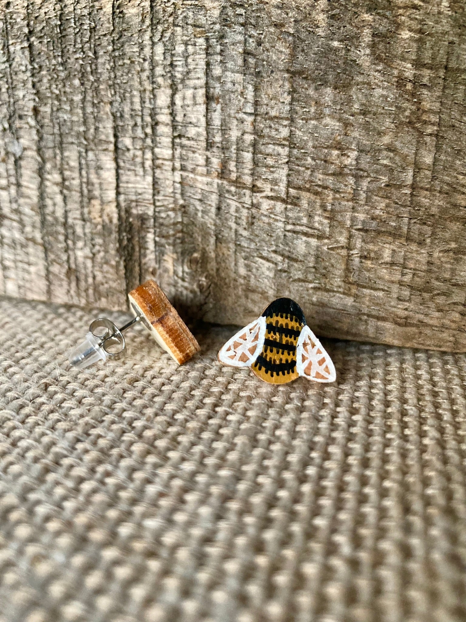 Side view of a bee cork stud earring showing the natural wood reverse and stainless steel post on a linen surface