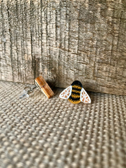 Side view of a bee cork stud earring showing the natural wood reverse and stainless steel post on a linen surface