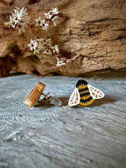 Side view of a bee cork stud earring on weathered wood showing the stainless steel post and silicone back against dried white blossom