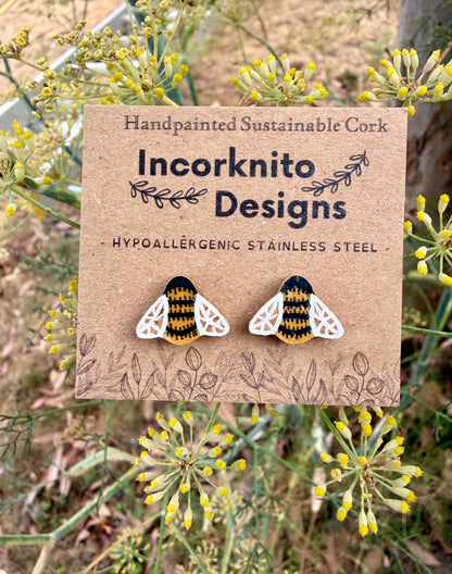 Handpainted bee cork stud earrings on an Incorknito Designs kraft card surrounded by yellow fennel flowers