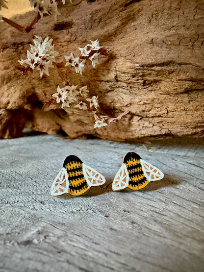 Pair of bee cork stud earrings on a weathered wood surface with dried white blossom