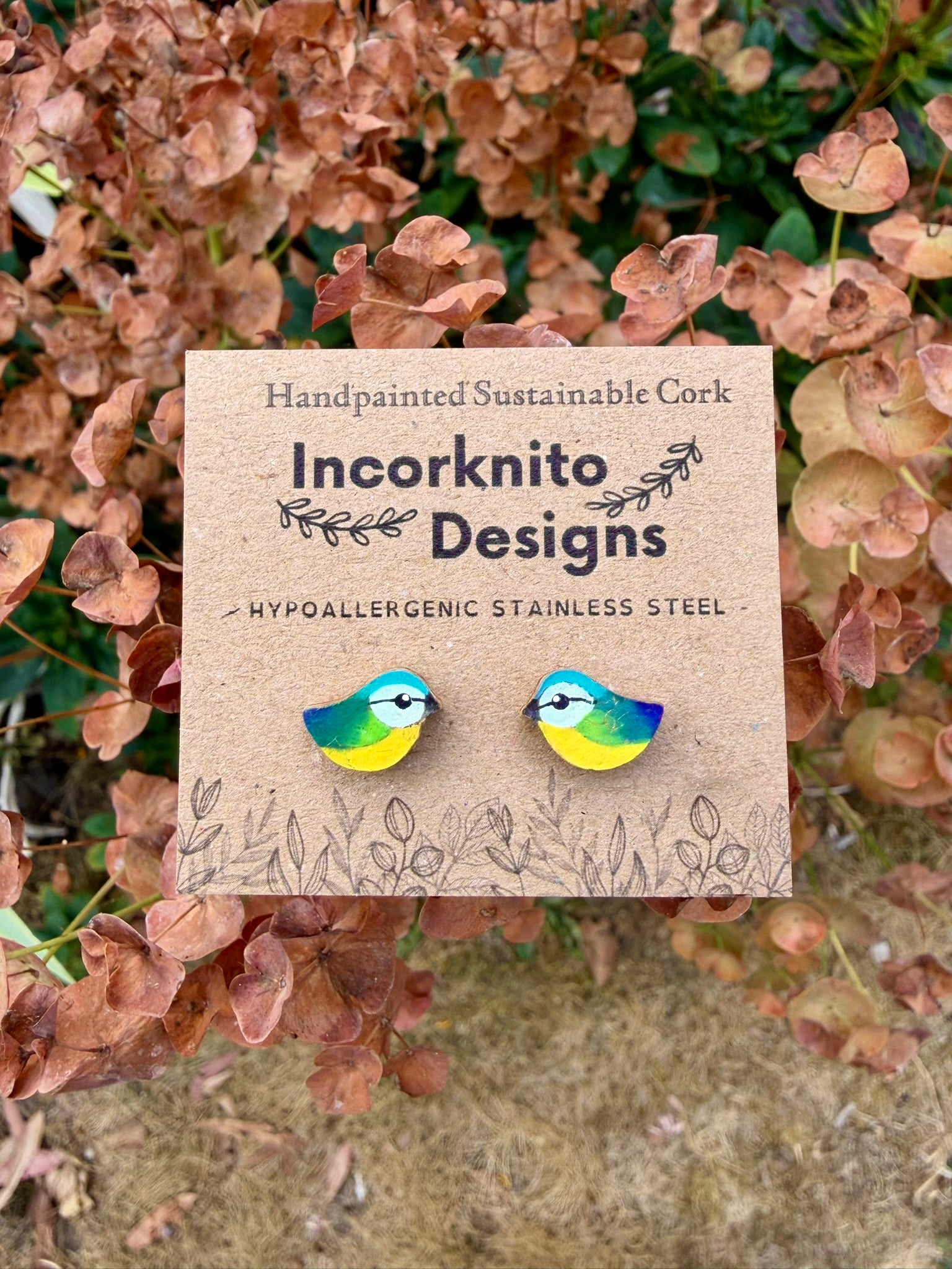 Blue tit cork stud earrings on an Incorknito Designs kraft card, displayed against copper-toned foliage
