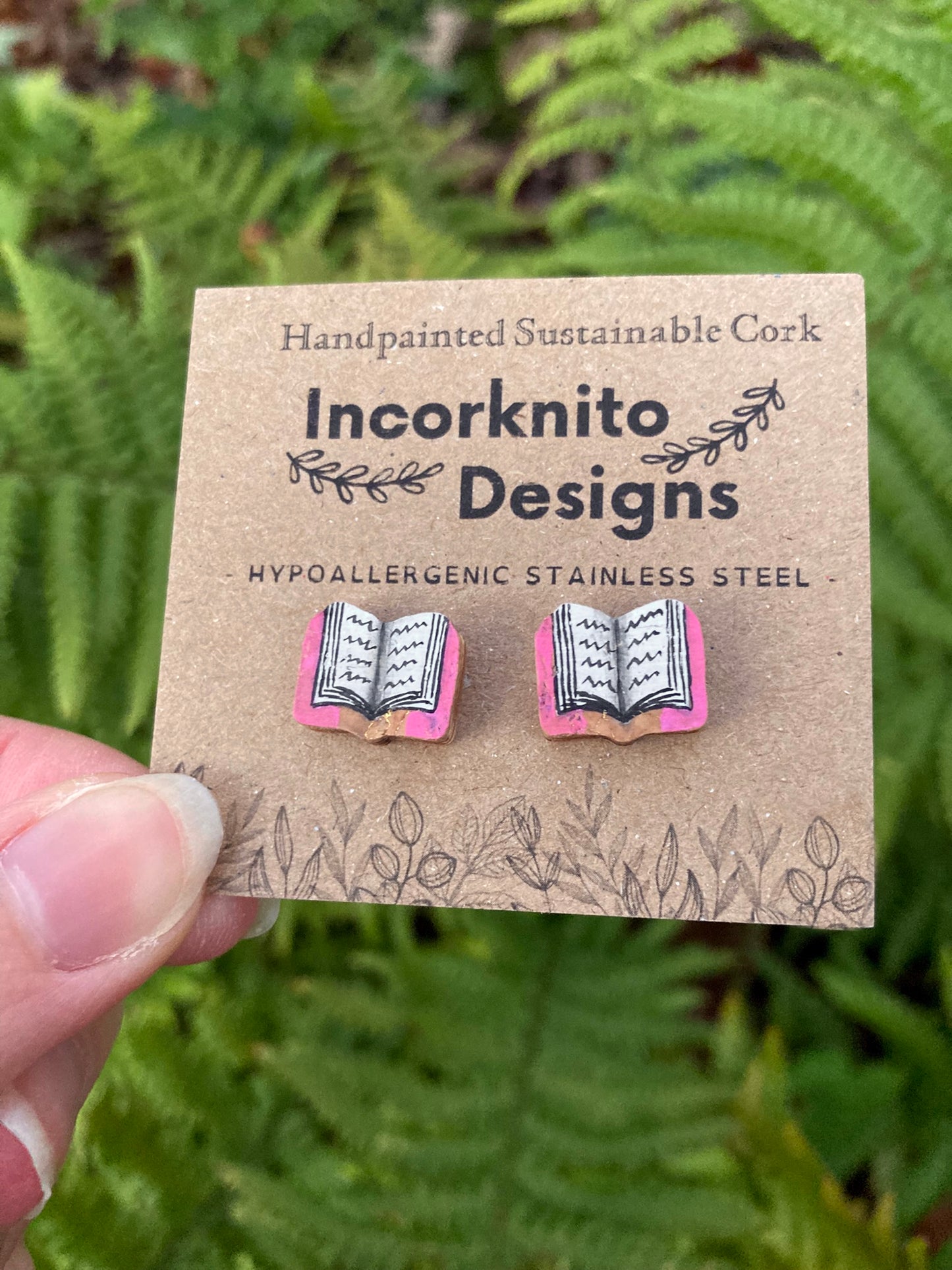 Pink handpainted book cork stud earrings on an Incorknito Designs kraft card held in hand showing scale