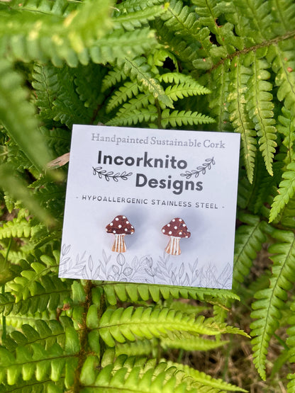Toadstool cork stud earrings on a branded card resting on a green leaf background