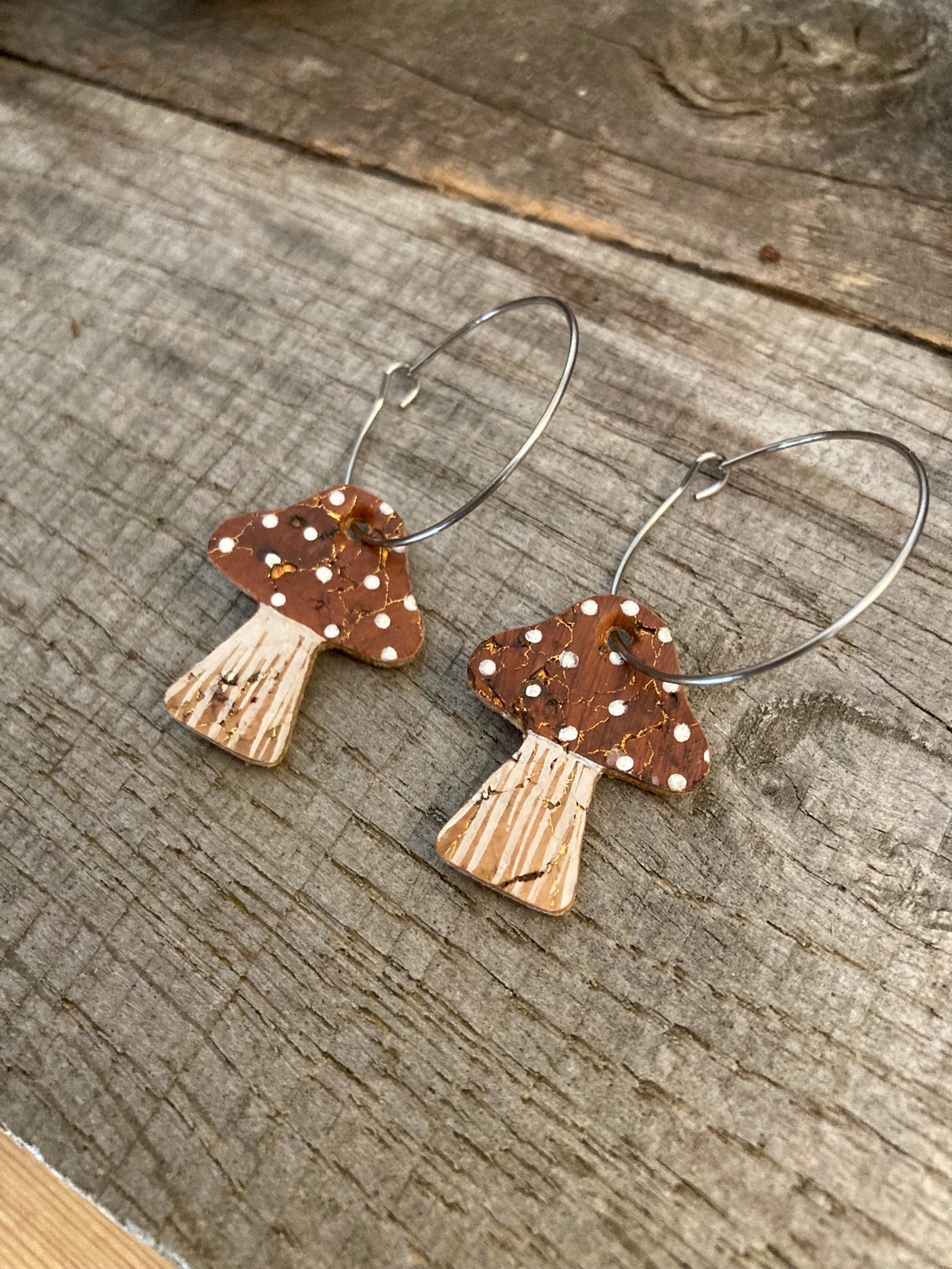 Brown toadstool cork large hoop earrings flat lay on plain weathered wood — editorial close-up showing the cork texture and gold fleck detail