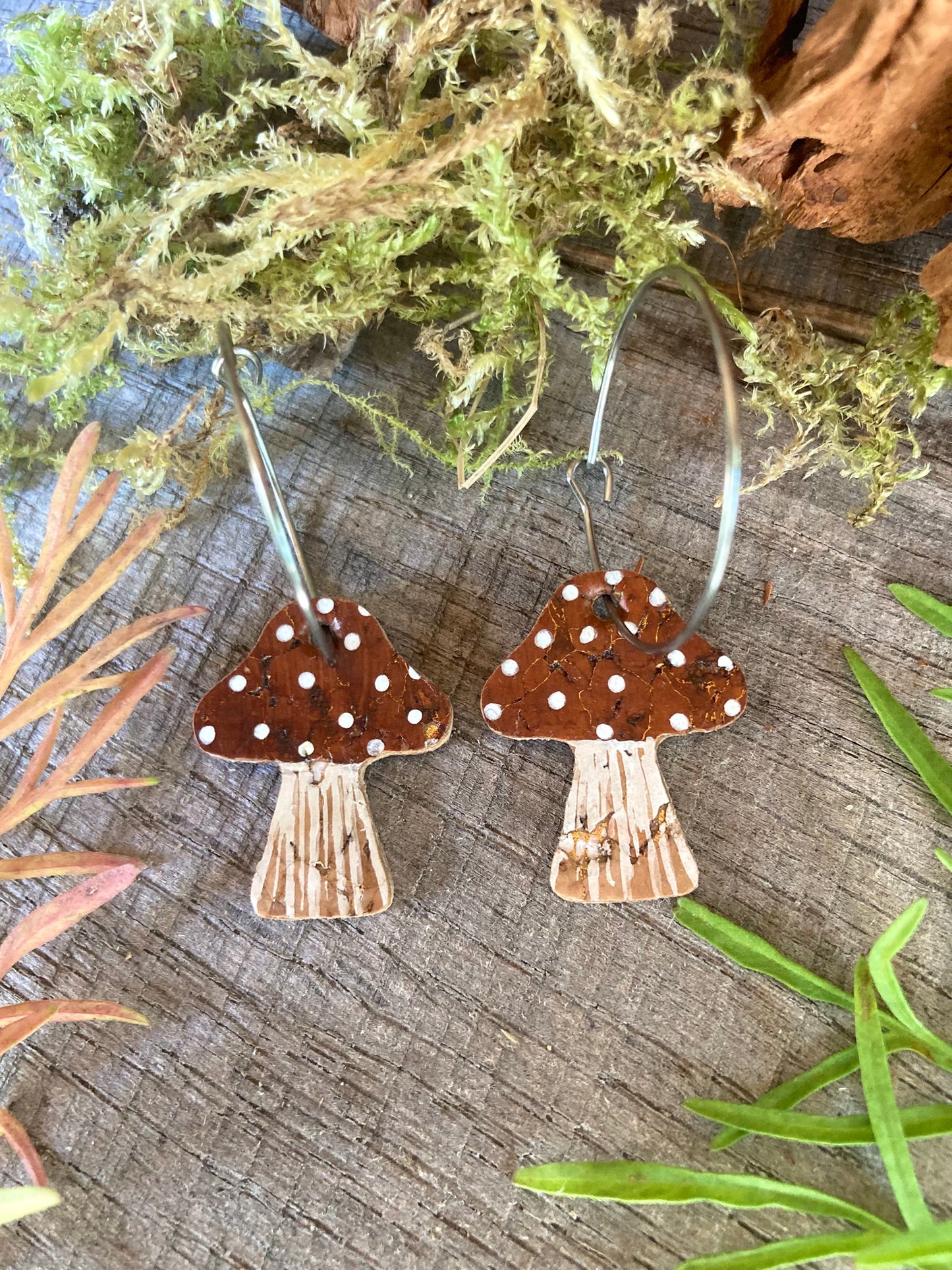Brown toadstool cork large hoop earrings flat lay on weathered wood — close-up showing the gold fleck cork texture and handpainted brown cap
