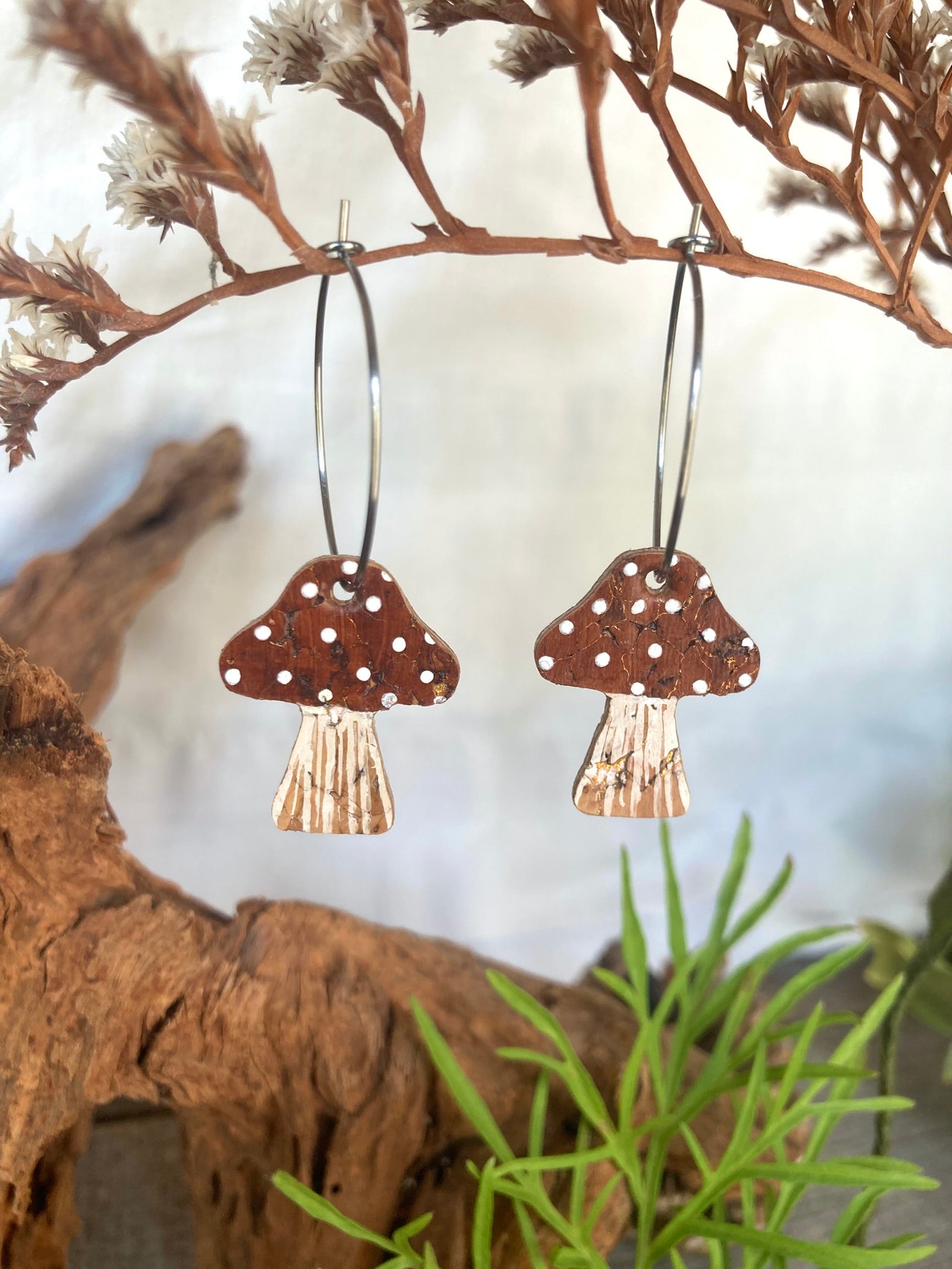 Brown toadstool cork large hoop earrings hanging from a dried branch — silver hoops with warm brown handpainted cap and white polka dots