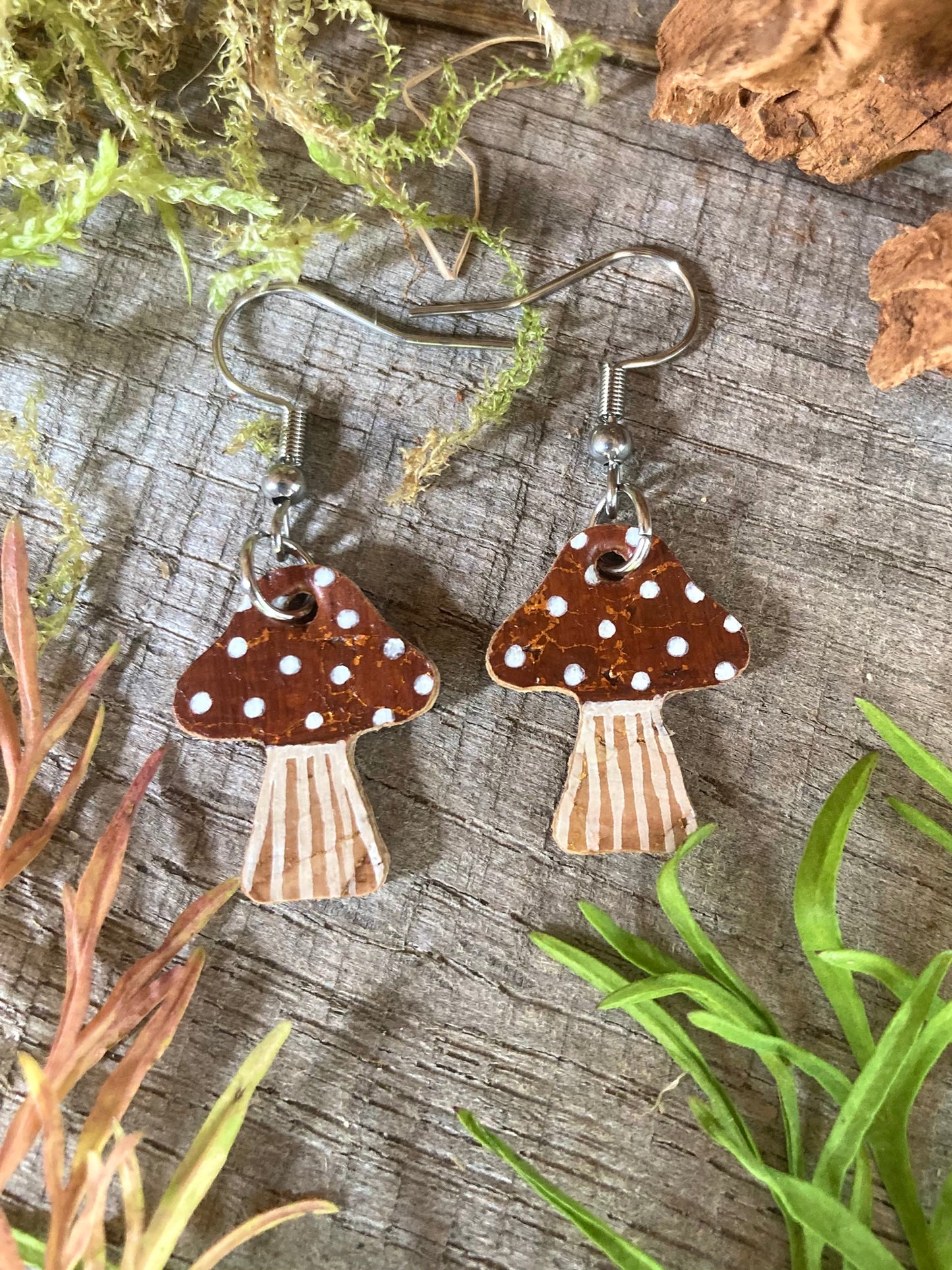 Brown toadstool cork medium earrings flat lay on weathered wood with moss and greenery — handpainted earthy brown cap with white spot detail