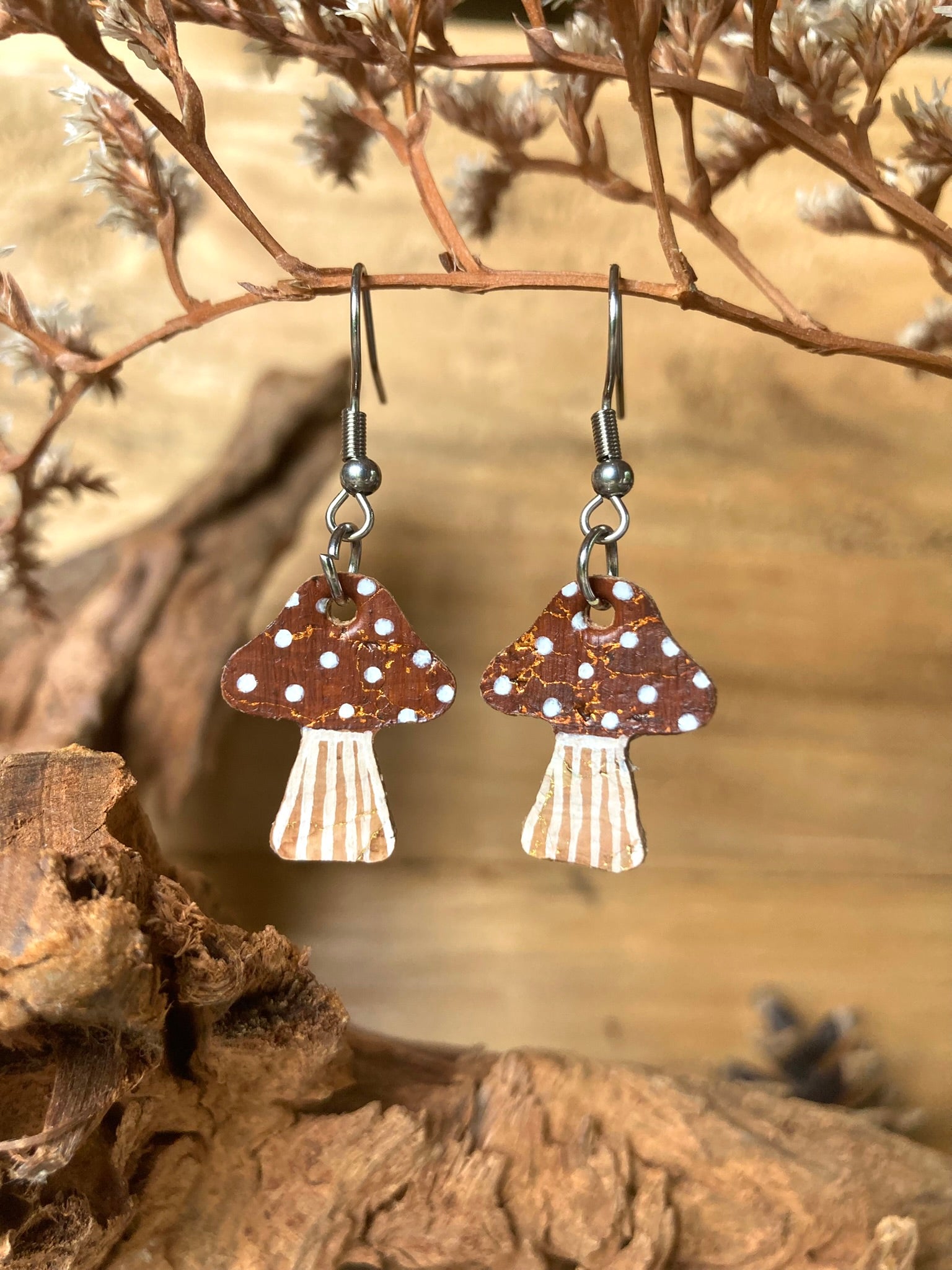 Brown toadstool cork medium earrings hanging from a dried branch — silver hooks with warm brown handpainted cap and white polka dots