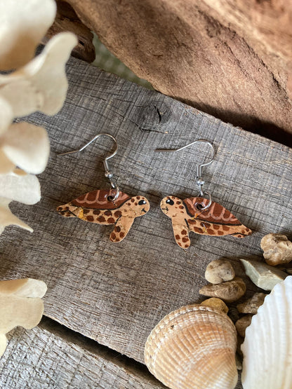 Brown handpainted cork sea turtle earrings with happy faces on a natural driftwood background — made in Suffolk UK