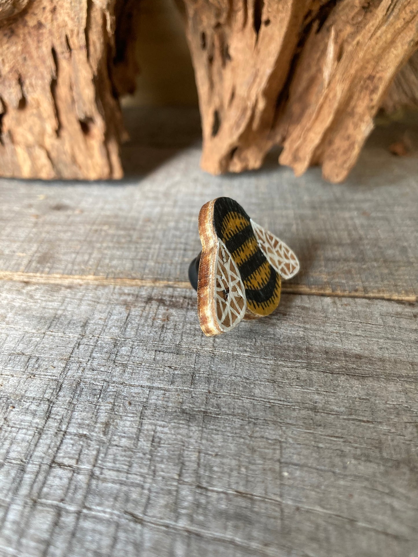 Angled view of the bumblebee cork pin badge on weathered wood showing cork top layer, FSC ply base and black rubber clasp