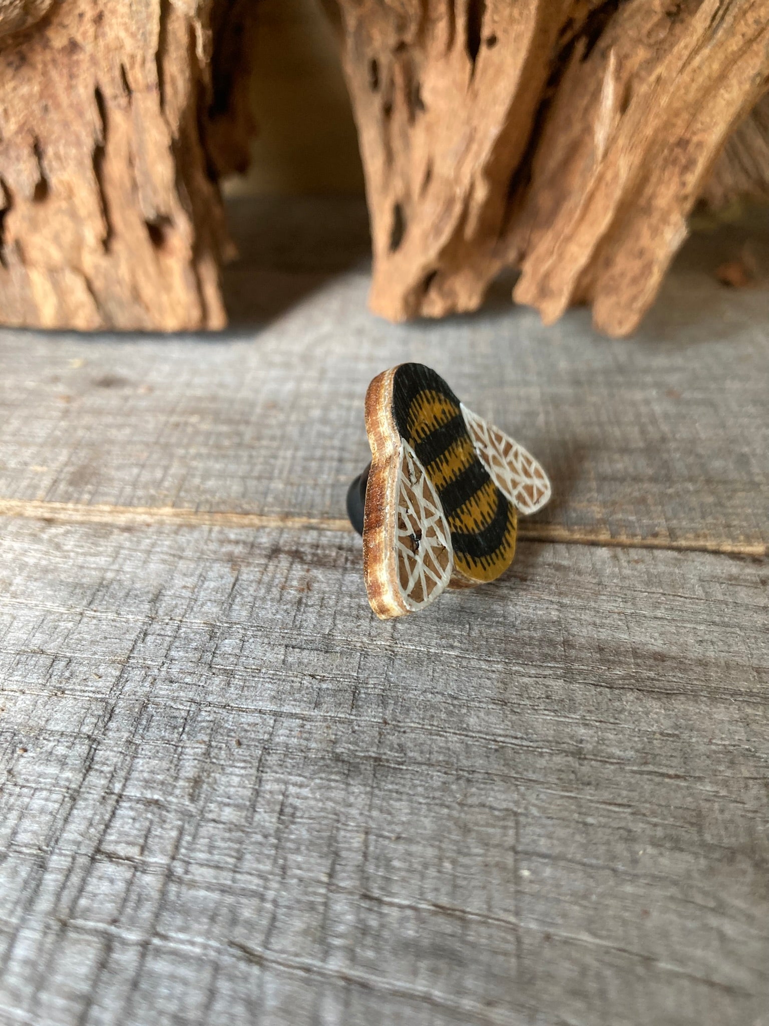 Angled view of the bumblebee cork pin badge on weathered wood showing cork top layer, FSC ply base and black rubber clasp