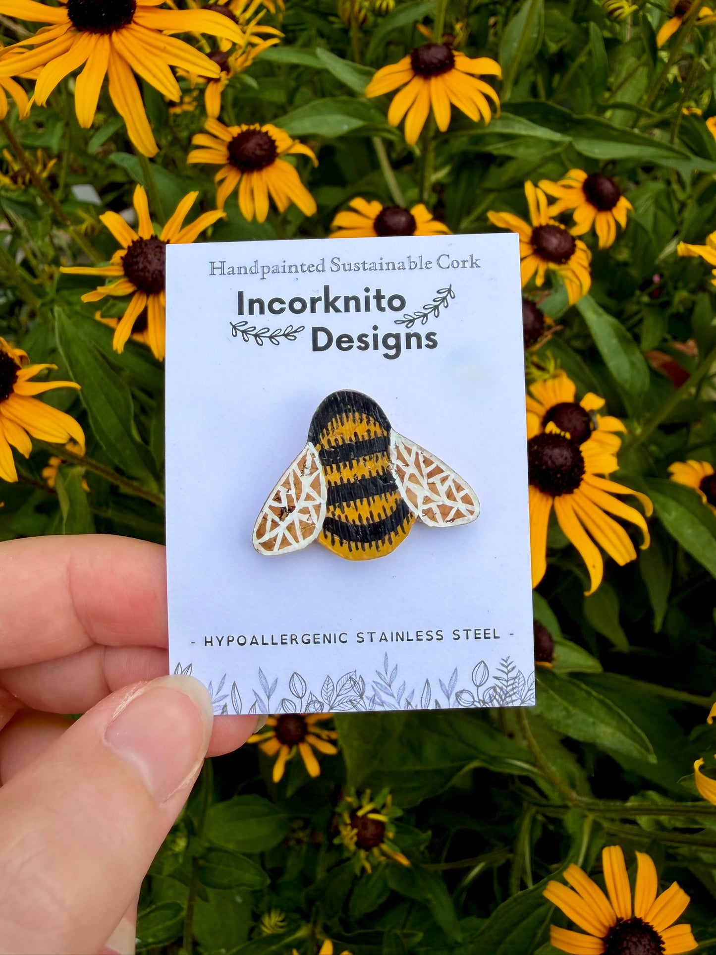 Bumblebee cork pin badge on Incorknito Designs branded card held against yellow rudbeckia flowers — handpainted sustainable cork badge