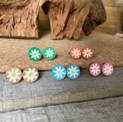 Handpainted daisy cork stud earrings in six colours — emerald, khaki, natural, orange, pink and light blue — on driftwood