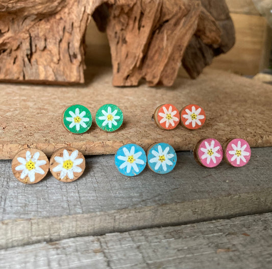 Handpainted daisy cork stud earrings in six colours — emerald, khaki, natural, orange, pink and light blue — on driftwood