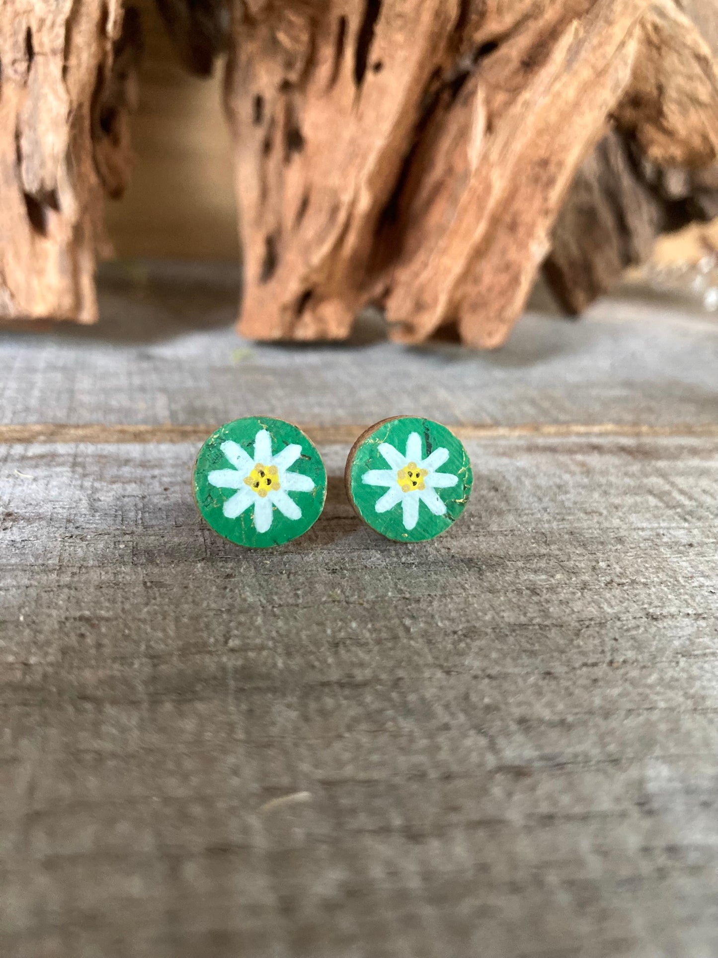 Emerald green daisy cork stud earrings with white petals and yellow centre on a wooden surface