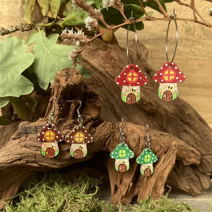 Fairy House Toadstool Earrings in red, green and brown — three colourways displayed together in a natural woodland setting with driftwood and moss