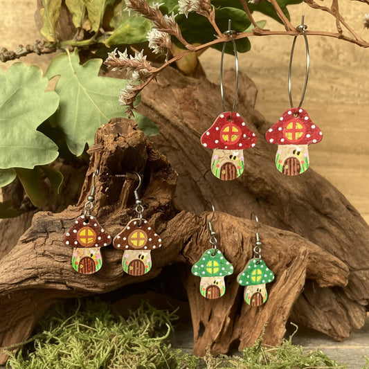 Fairy House Toadstool Earrings in red, green and brown — three colourways displayed together in a natural woodland setting with driftwood and moss