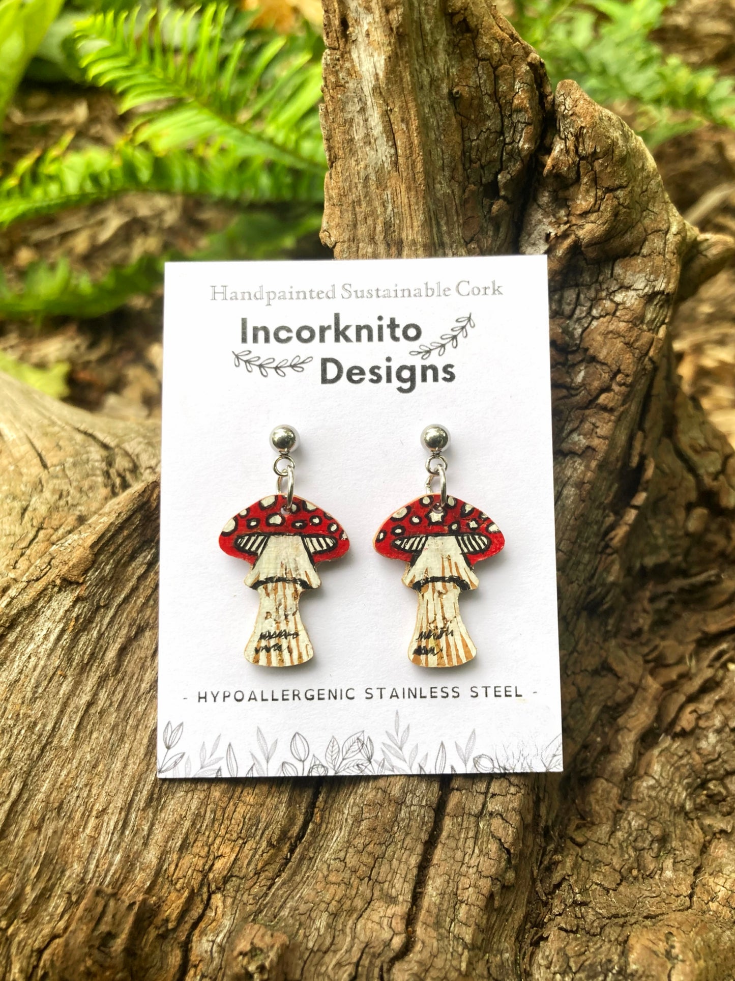 Fly agaric toadstool cork earrings on silver ball studs on Incorknito Designs card against mossy bark and green ferns — handpainted eco-friendly jewellery