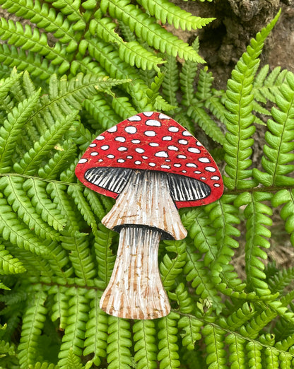Handpainted fly agaric toadstool cork bookmark against lush green ferns — bold red cap with white spots and fine gill detail, handmade in Suffolk UK