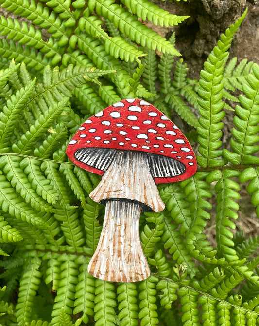 Handpainted fly agaric toadstool cork bookmark against lush green ferns — bold red cap with white spots and fine gill detail, handmade in Suffolk UK