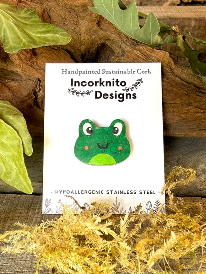 Orange cheeked frog cork pin badge on Incorknito Designs branded card against driftwood and dried moss