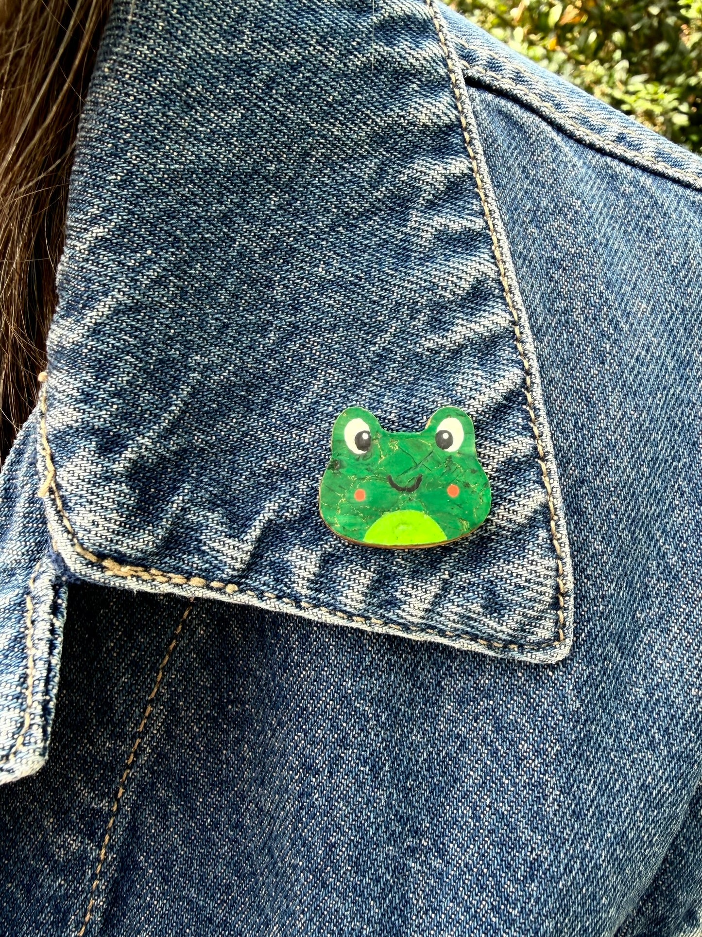 Orange cheeked frog cork pin badge pinned to a denim jacket — handpainted smiley frog face, sustainable cork badge